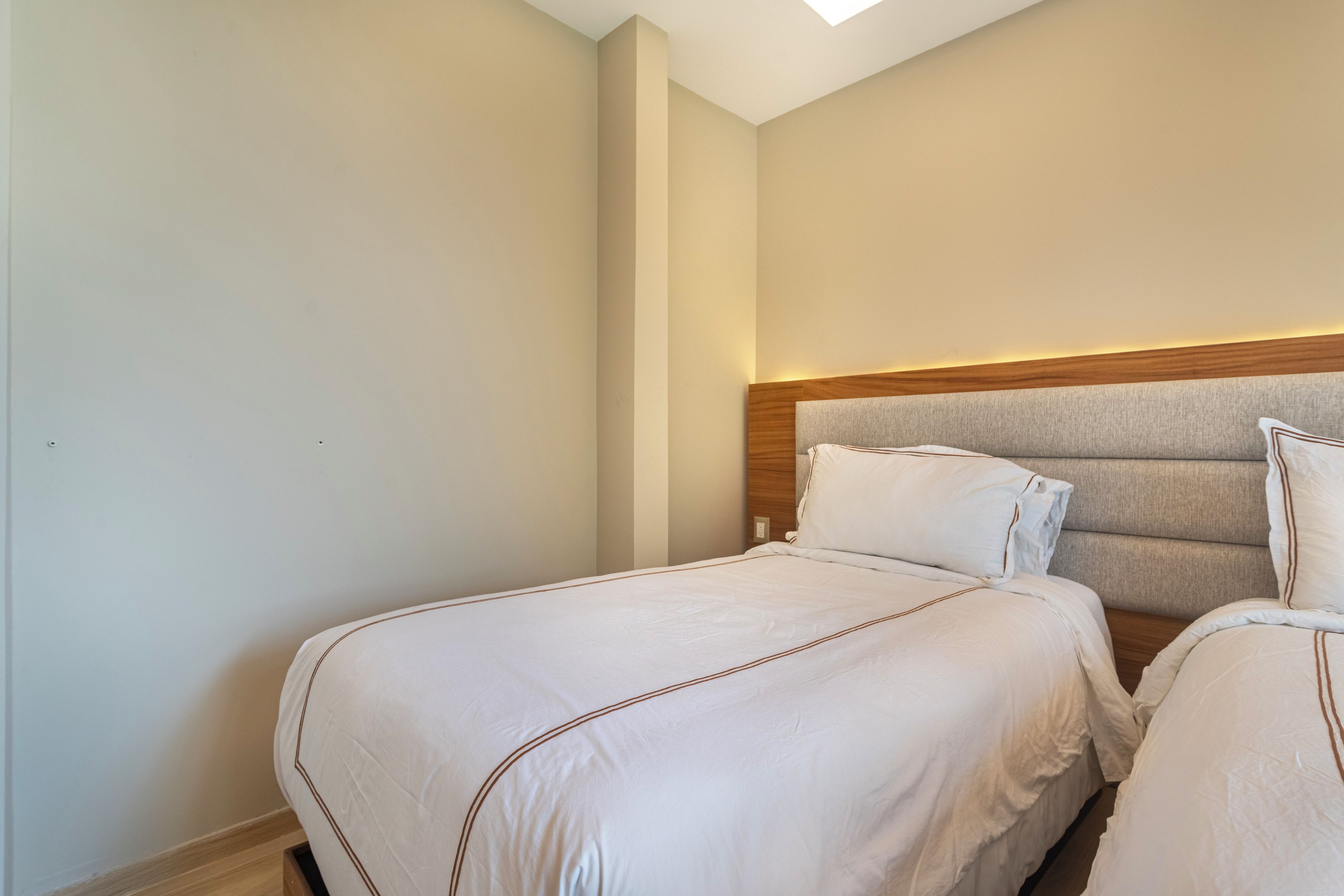 Quarto de hotel com duas camas, cabeceira de madeira e luminária no teto.