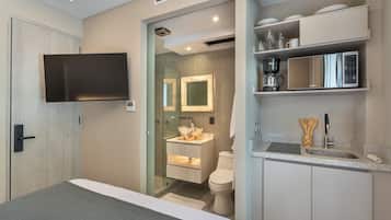 Habitación de hotel moderna con cama, televisor, baño con lavamanos e inodoro, y un área de cocina con microondas.