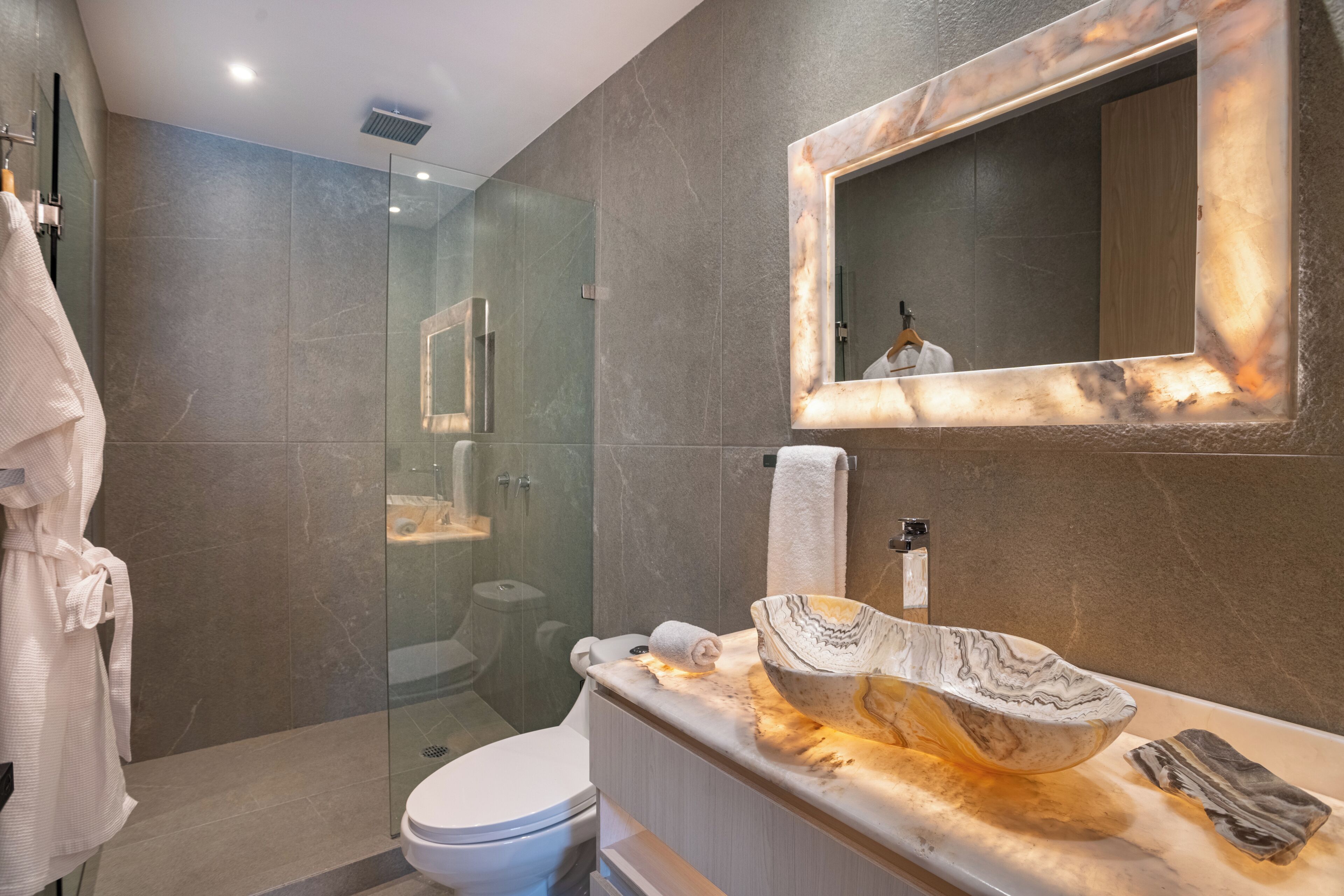 Un baño moderno con ducha envuelta en vidrio, lavamanos de mármol y un espejo grande.