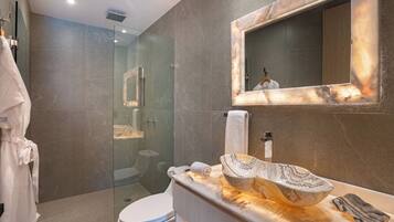 Un baño moderno con ducha envuelta en vidrio, lavamanos de mármol y un espejo grande.