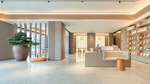 A modern lobby with a reception desk, a large potted plant, and a bookshelf.