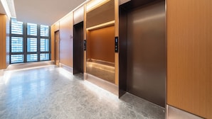 A modern elevator area with a marble floor, wooden paneling, and a view through the windows.