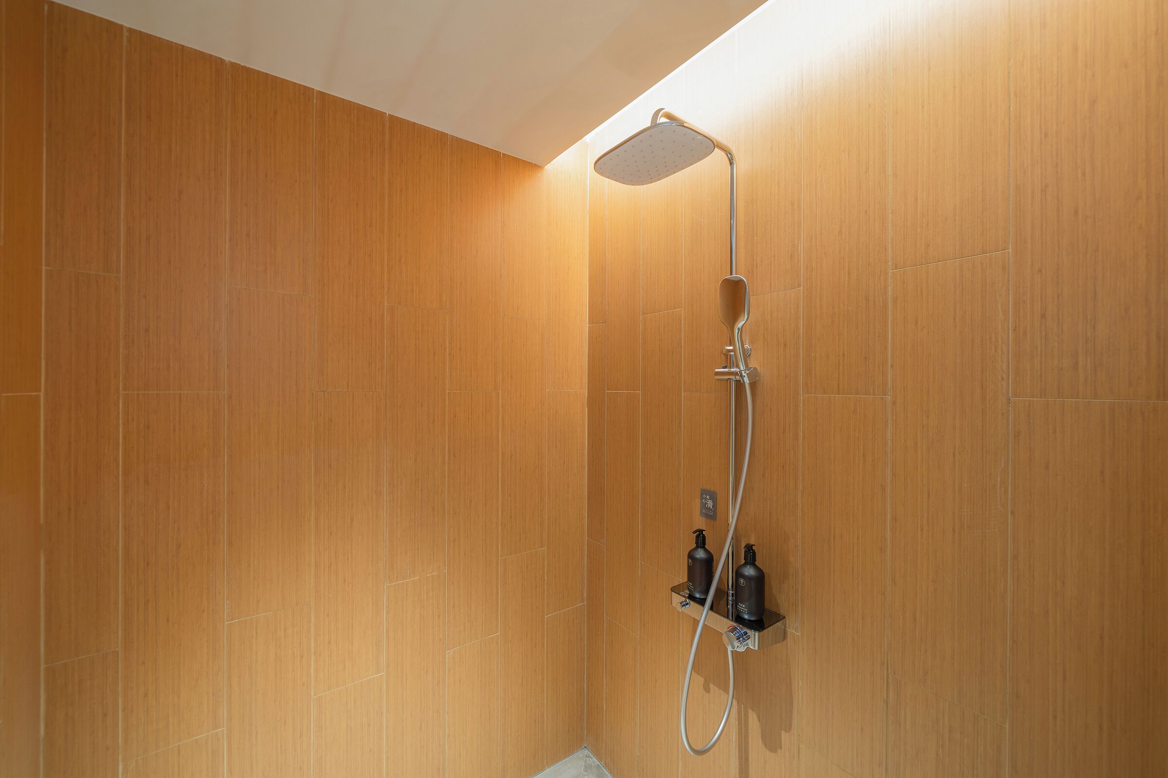 A shower with a handheld showerhead, a wall-mounted control panel, and a shelf with toiletries.
