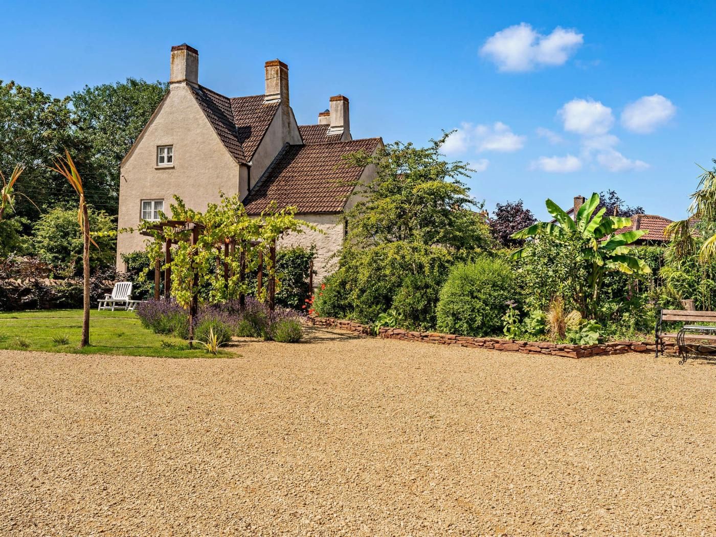 A large house with a gravel driveway, surrounded by lush greenery and a well-maintained garden.