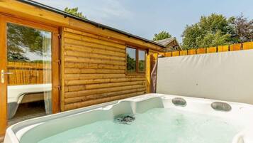 Un bain à remous dans un chalet en bois, avec une porte vitrée donnant sur un espace patio.