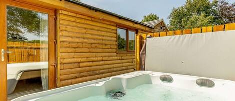 Un jacuzzi en una cabaña de madera con un ventanal que da a un patio.