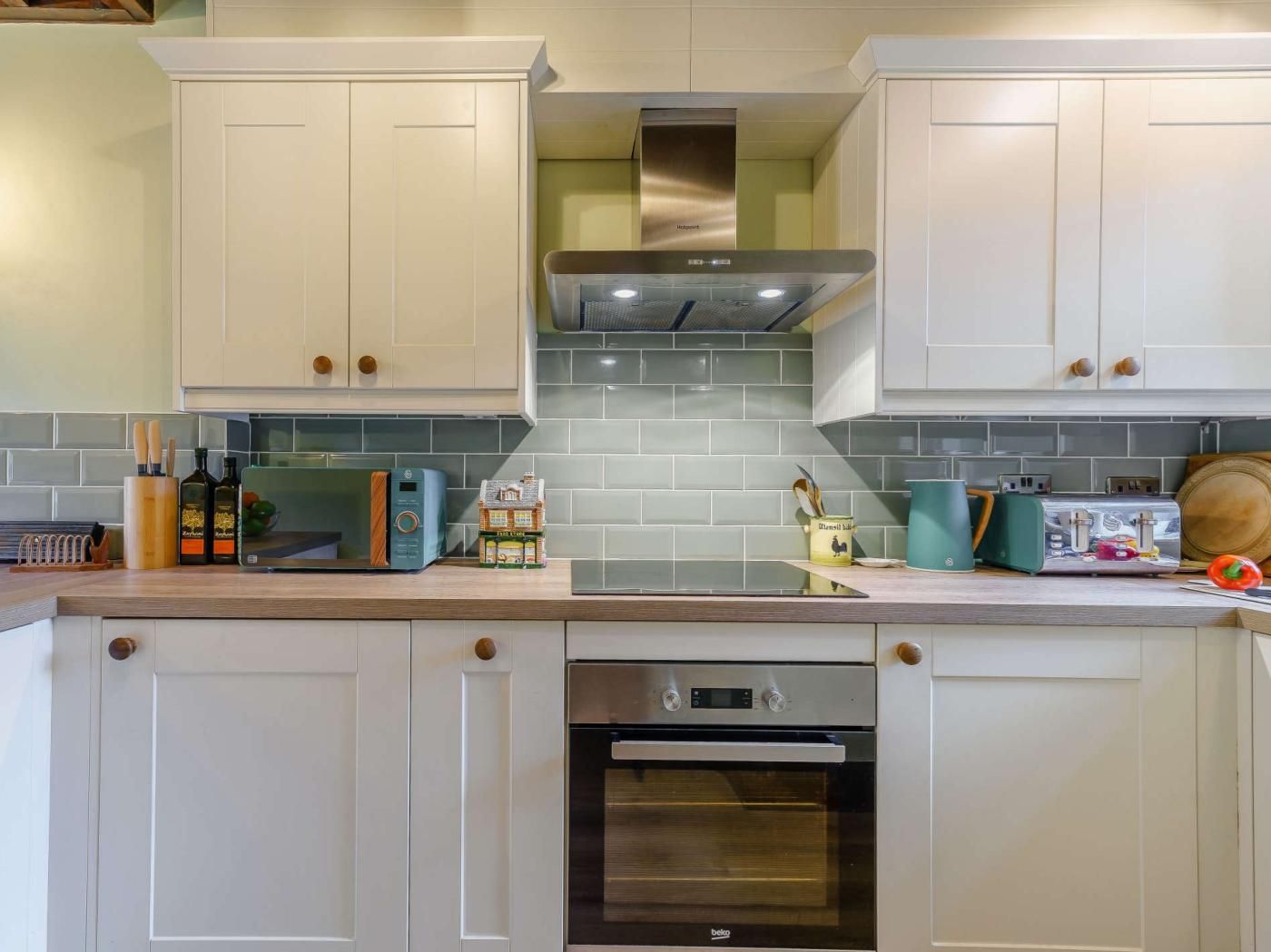 A kitchen with white cabinets, a stainless steel range hood, a built-in oven, and a tiled backsplash.