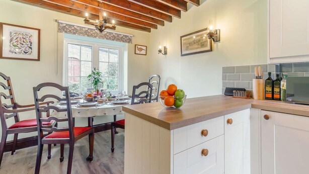 Een keuken met witte kasten, een houten plafond en een eethoek met stoelen en een tafel.