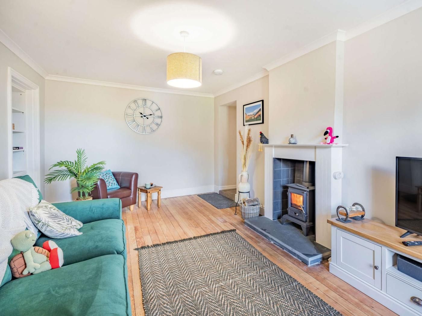 A living room with a sofa, a fireplace, a television, and a clock on the wall.