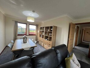 A dining area with a table and chairs, a sofa, a bookshelf, and a view through the window. - 3 Bed in Newton Stewart (oc-87541) (Mochrum)