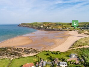 An aerial view of a coastal area with a sandy beach, green fields, and a few buildings. - 2 Bed in Braunton (oc-87755) (Croyde)