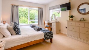 Ein Schlafzimmer mit Bett, Schreibtisch, Kommode, Fernseher und einem Fenster mit Vorhängen.