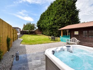 Ein Garten mit Whirlpool, Rasenfläche, Holzzaun und Holzbauten.