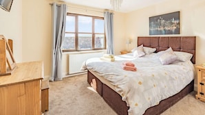 Ein Schlafzimmer mit einem großen Bett, einem Fenster mit Vorhängen, einem Heizkörper, einem hölzernen Nachttisch und einem Bild an der Wand.