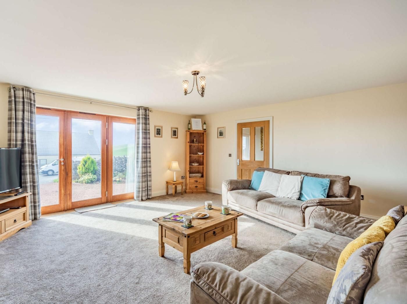 A living room with a sofa, a coffee table, a television, a bookshelf, and a sliding glass door leading to a garden.