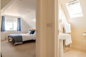 Ein Schlafzimmer mit Bett, einem Fenster mit Vorhängen, einem Heizkörper und einem Badezimmer mit Waschbecken und Handtuchhalter.