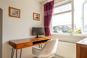 Ein Zimmer mit einem Holztisch, einem Computermonitor, einem weißen Stuhl und einem Fenster mit Blick auf Häuser.