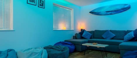 A living room with a sofa, bean bags, a coffee table, and a wall-mounted artwork.