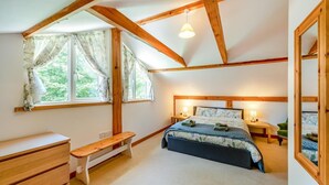 Ein Schlafzimmer mit einem Bett, Nachttischen, einer Bank, einer Kommode und einem Fenster mit Vorhängen.