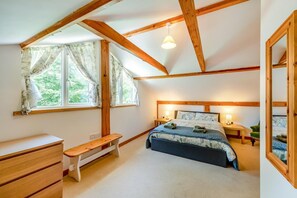 Ein Schlafzimmer mit einem Bett, Nachttischen, einer Bank, einer Kommode und einem Fenster mit Vorhängen.