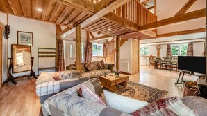 Ein geräumiges Wohnzimmer mit hoher Holzbalkendecke, einer Sofagarnitur, einem Couchtisch und einem Fernseher.