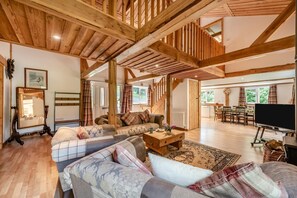 Ein geräumiges Wohnzimmer mit hoher Holzbalkendecke, einer Sofagarnitur, einem Couchtisch und einem Fernseher.