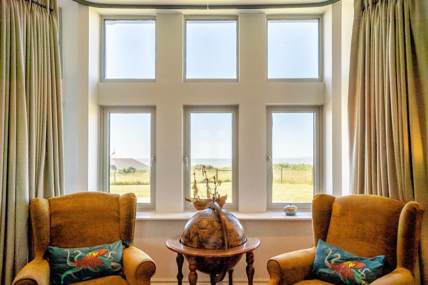 Ein Zimmer mit einem großen Fenster, zwei Sesseln, einem kleinen Tisch mit einer Dekoration und Vorhängen.