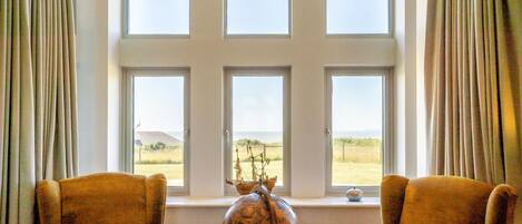 Ein Zimmer mit einem großen Fenster, zwei Sesseln, einem kleinen Tisch mit einer Dekoration und Vorhängen.