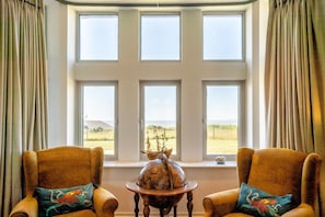 A room with a large window, two armchairs, a small table with a decorative item, and curtains.