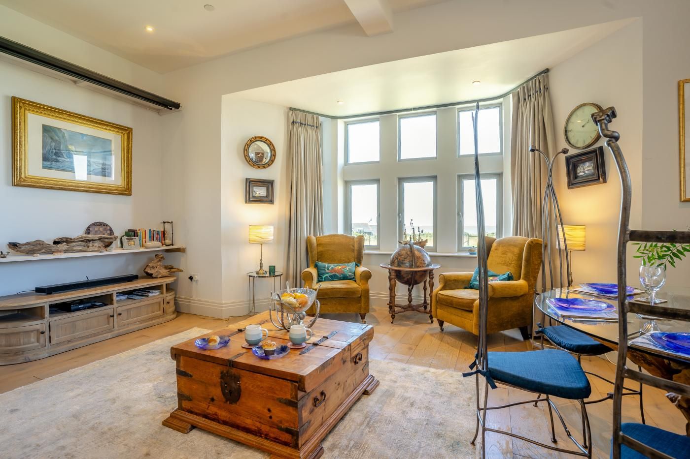A living room with a wooden coffee table, two armchairs, a sideboard, and a large window with curtains.