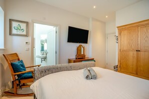 A bedroom with a bed, a wooden wardrobe, a television, a chair, and a bathroom visible through an open door.