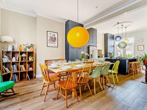 A dining area with a wooden table set for four, surrounded by chairs, a bookshelf, and a hanging light fixture.