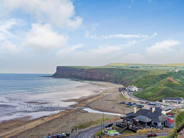 A coastal town with a beach, a road curving around the town, and buildings with visible signage.