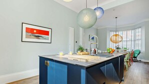 Eine moderne Küche mit einer zentralen Kochinsel, Pendelleuchten und Blick ins Freie durch große Fenster.