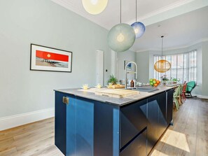 A modern kitchen with a central island, pendant lighting, and a view of the outdoors through large windows.
