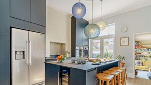 Eine moderne Küche mit integrierter Kochinsel, Barhocker, Wasserspender und Blick ins Freie.