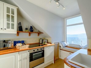 Une cuisine compacte avec des meubles blancs, un four encastré et une fenêtre donnant sur la mer.