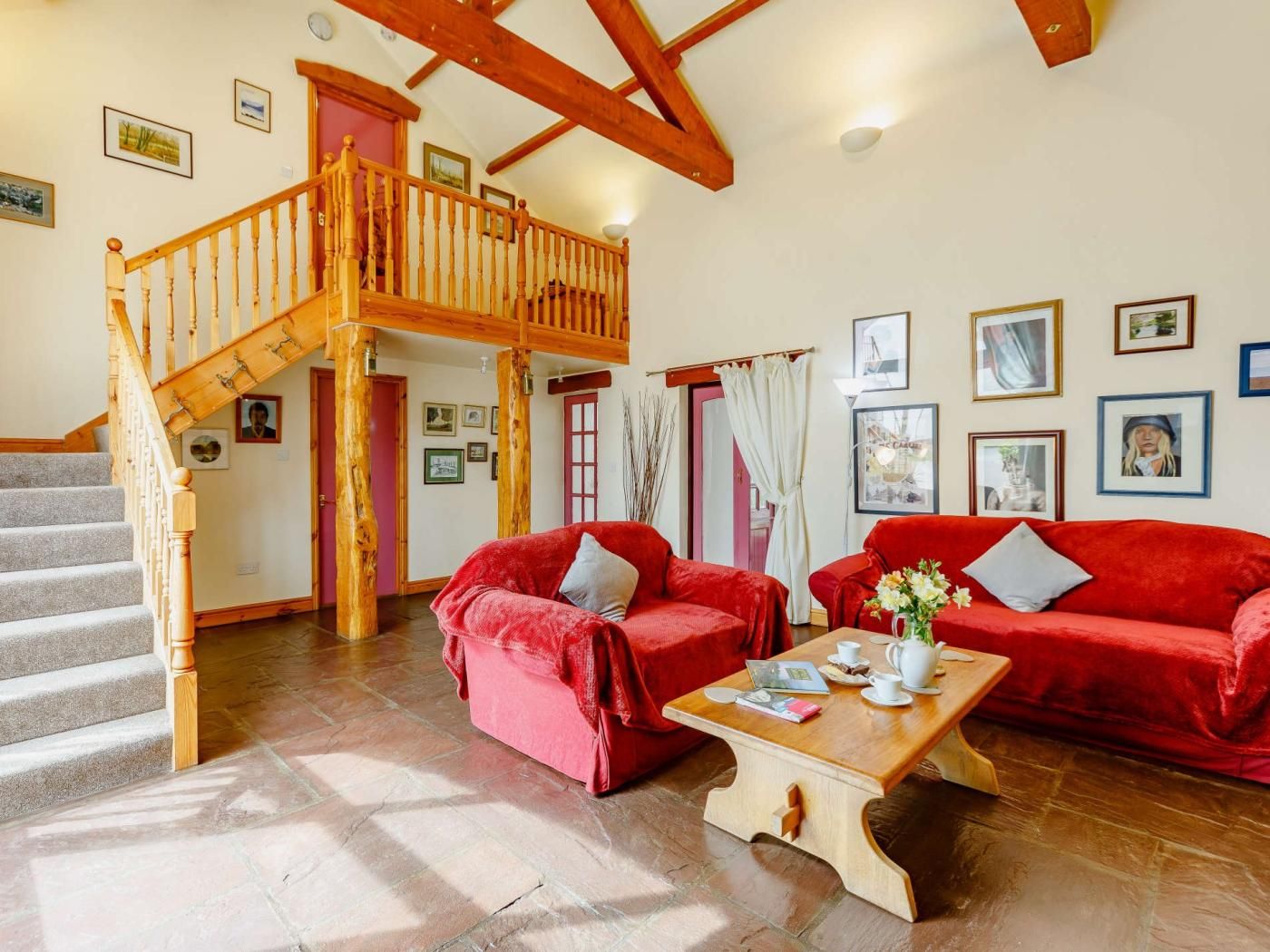 A spacious living area with a wooden staircase, red sofas, a coffee table, and a view of a red door.