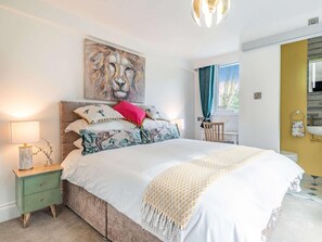 Ein Schlafzimmer mit Bett, Nachttisch, einem Gemälde, einem Fenster und einem Badezimmer im Hintergrund.