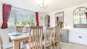 A dining room with a wooden table and chairs, a chandelier, a window with curtains, and a mirror on the wall. - 4 Bed in Bakewell (oc-87419) (Bakewell)