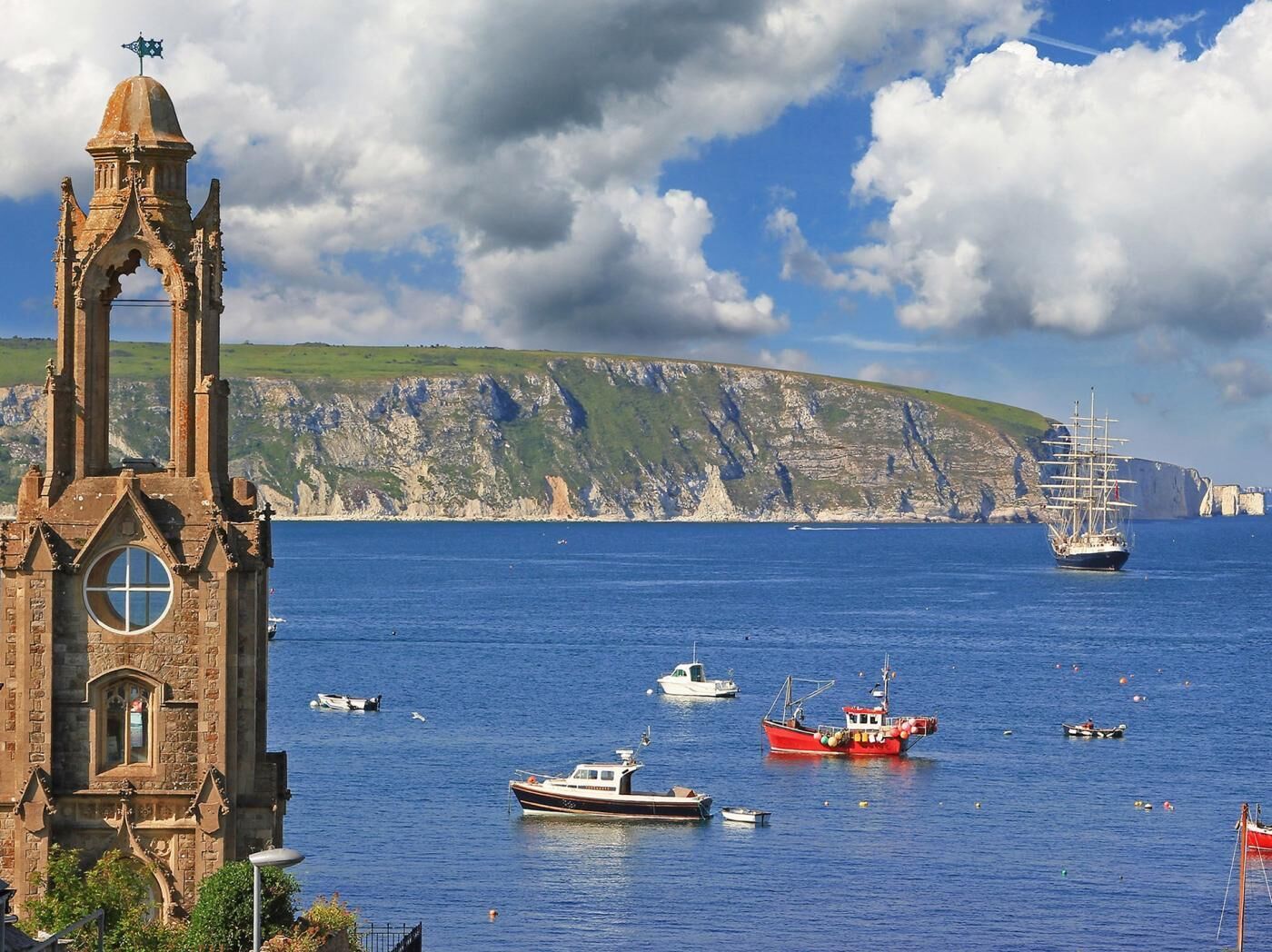 A coastal scene with a historic tower, boats, and cliffs.