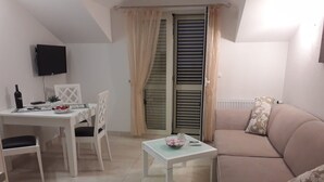 A living room with a sofa, a coffee table, a dining table with chairs, a TV mounted on the wall, and a window with curtains. - Deluxe Two Bedroom Apartment with Terrace (Supetar)