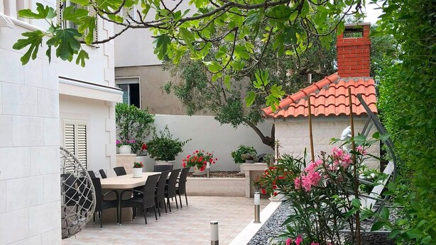 A patio with a table and chairs, surrounded by potted plants and a small garden area. - Deluxe Two Bedroom Apartment with Terrace (Supetar)