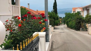 A residential street with a white building, a red-tiled roof, and a row of red flowers along the fence. - Deluxe Two Bedroom Apartment with Terrace (Supetar)