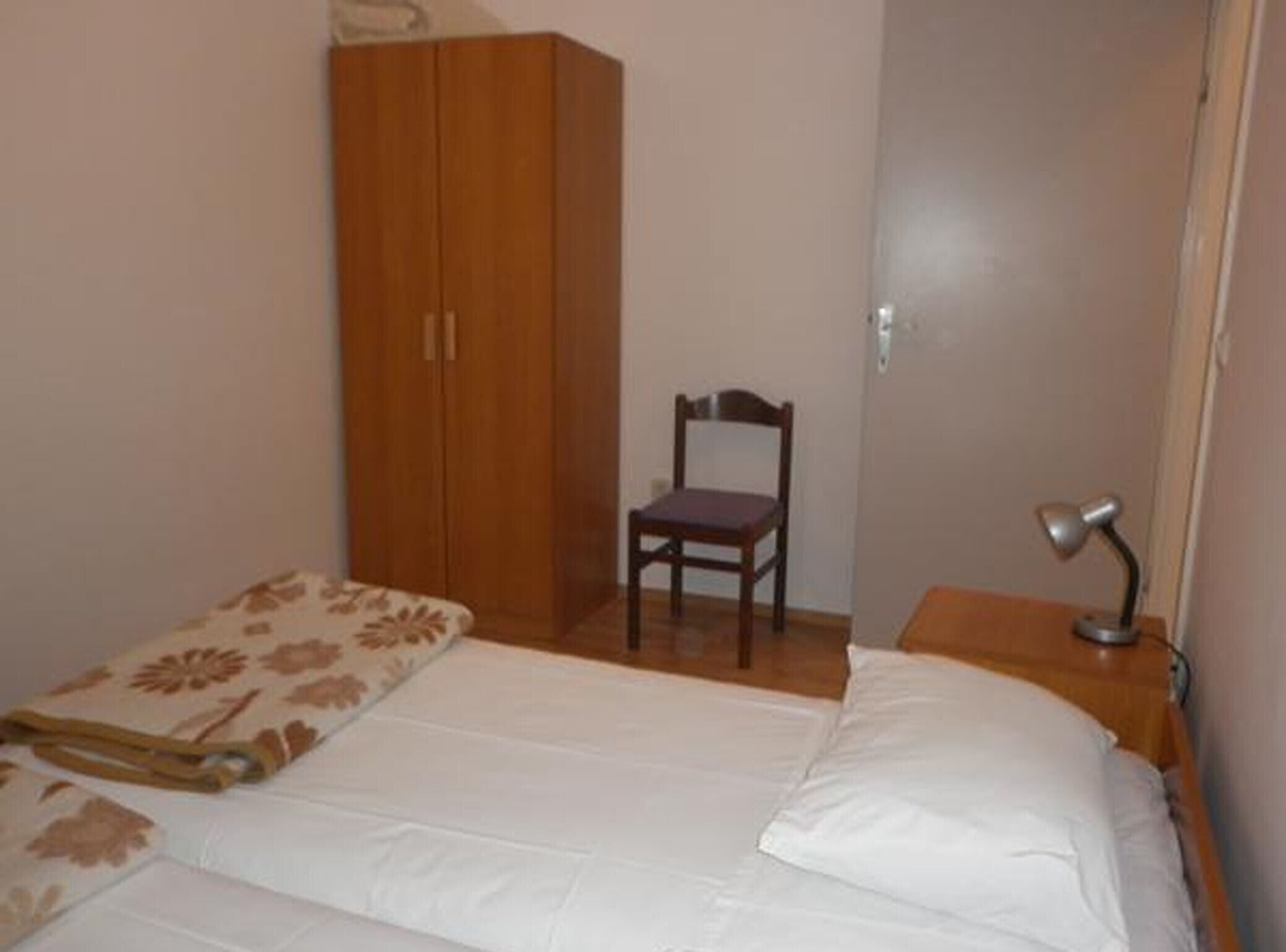 Una camera da letto con un letto, un armadio in legno, una sedia e una scrivania con una lampada.
