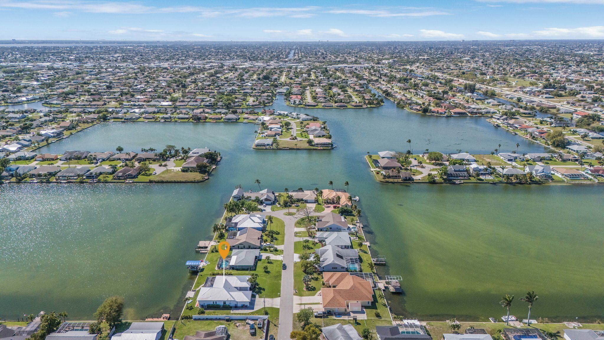 An aerial view of a residential area with houses, water bodies, and a central road.
