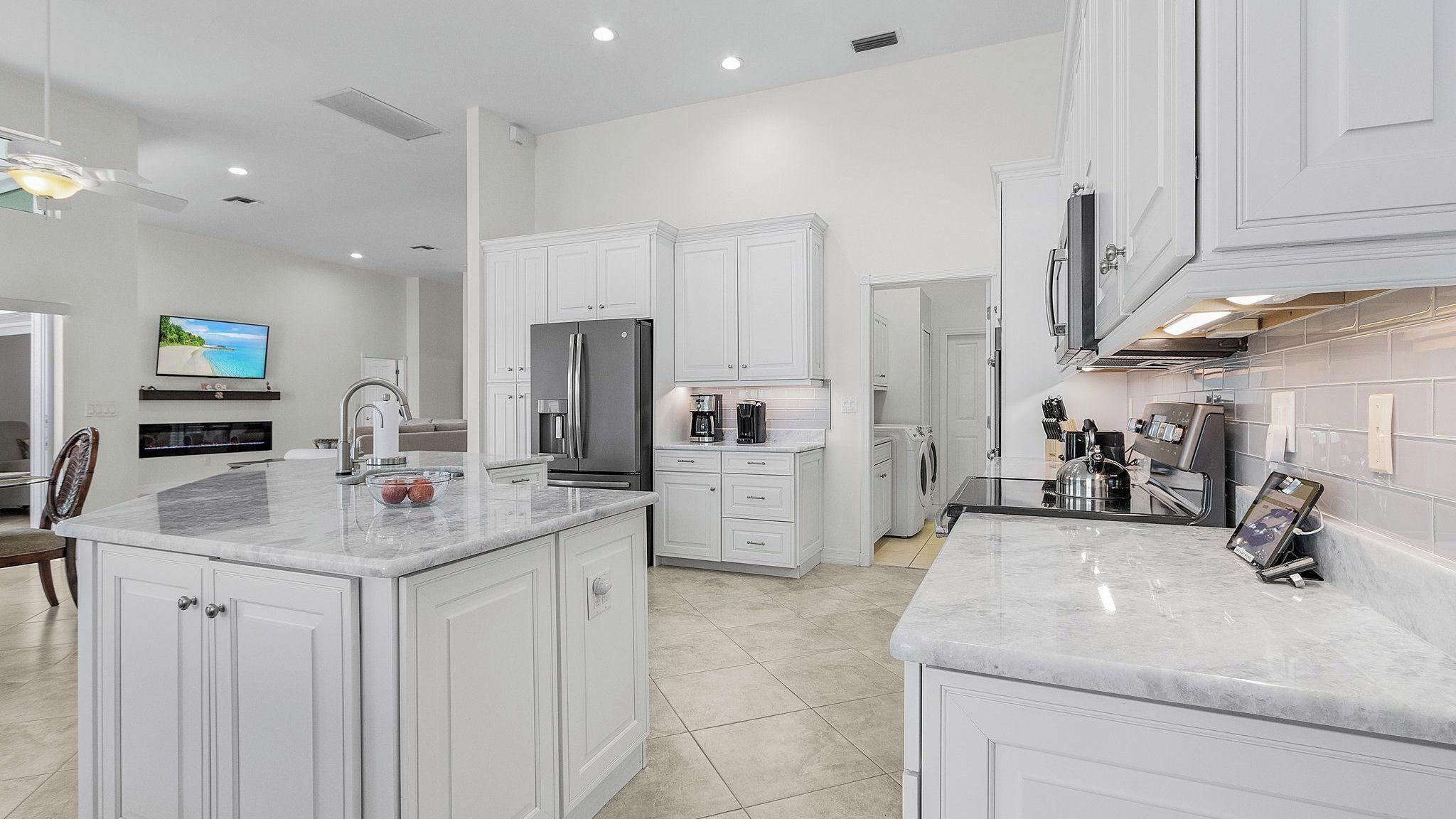 A modern kitchen with white cabinetry, a large island, a built-in refrigerator, and a coffee maker.