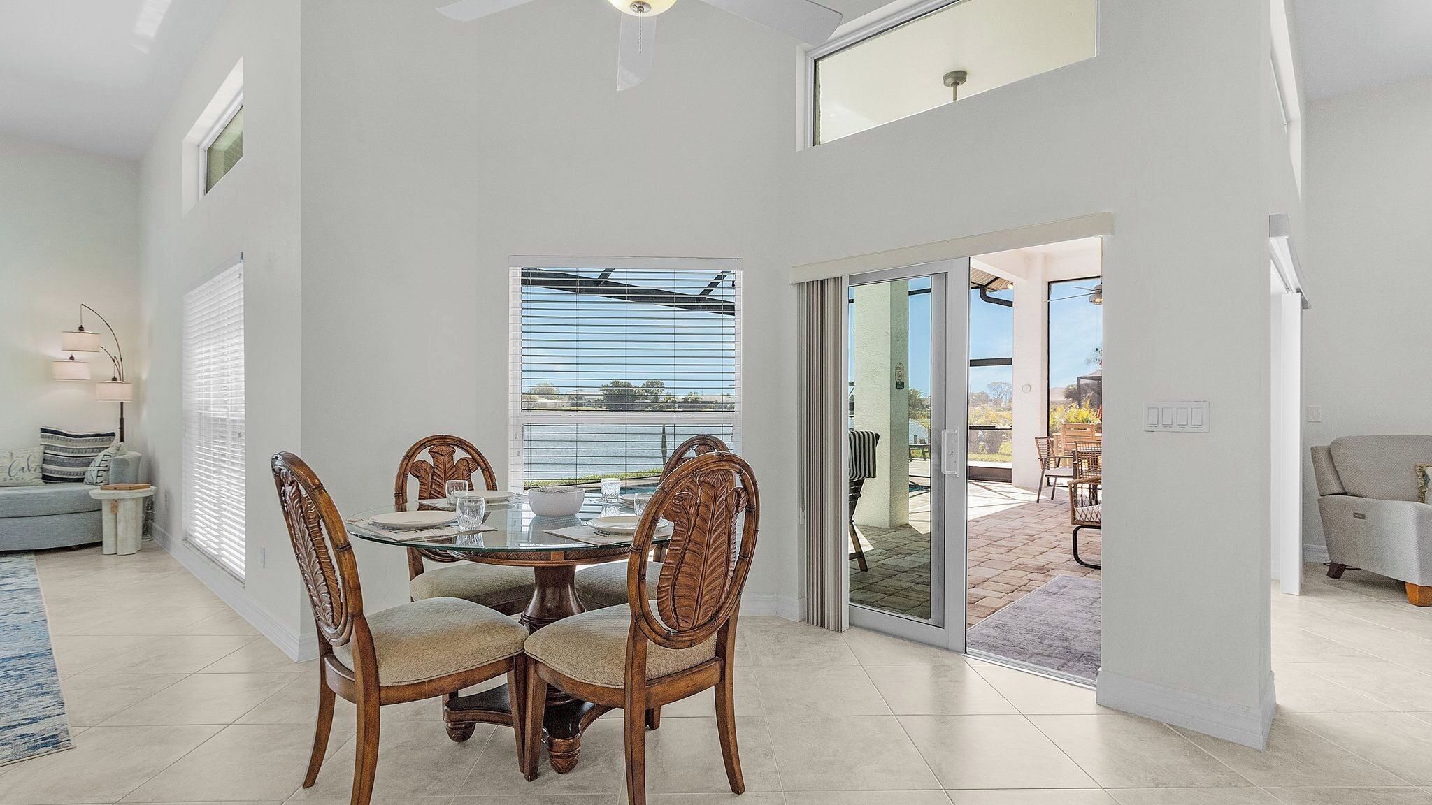 A dining area with a glass table and wooden chairs, a sofa, and a view through a window.