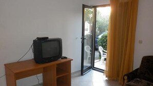 Une pièce avec un téléviseur posé sur un meuble en bois, une porte-fenêtre coulissante donnant sur l’extérieur et un fauteuil à motifs.