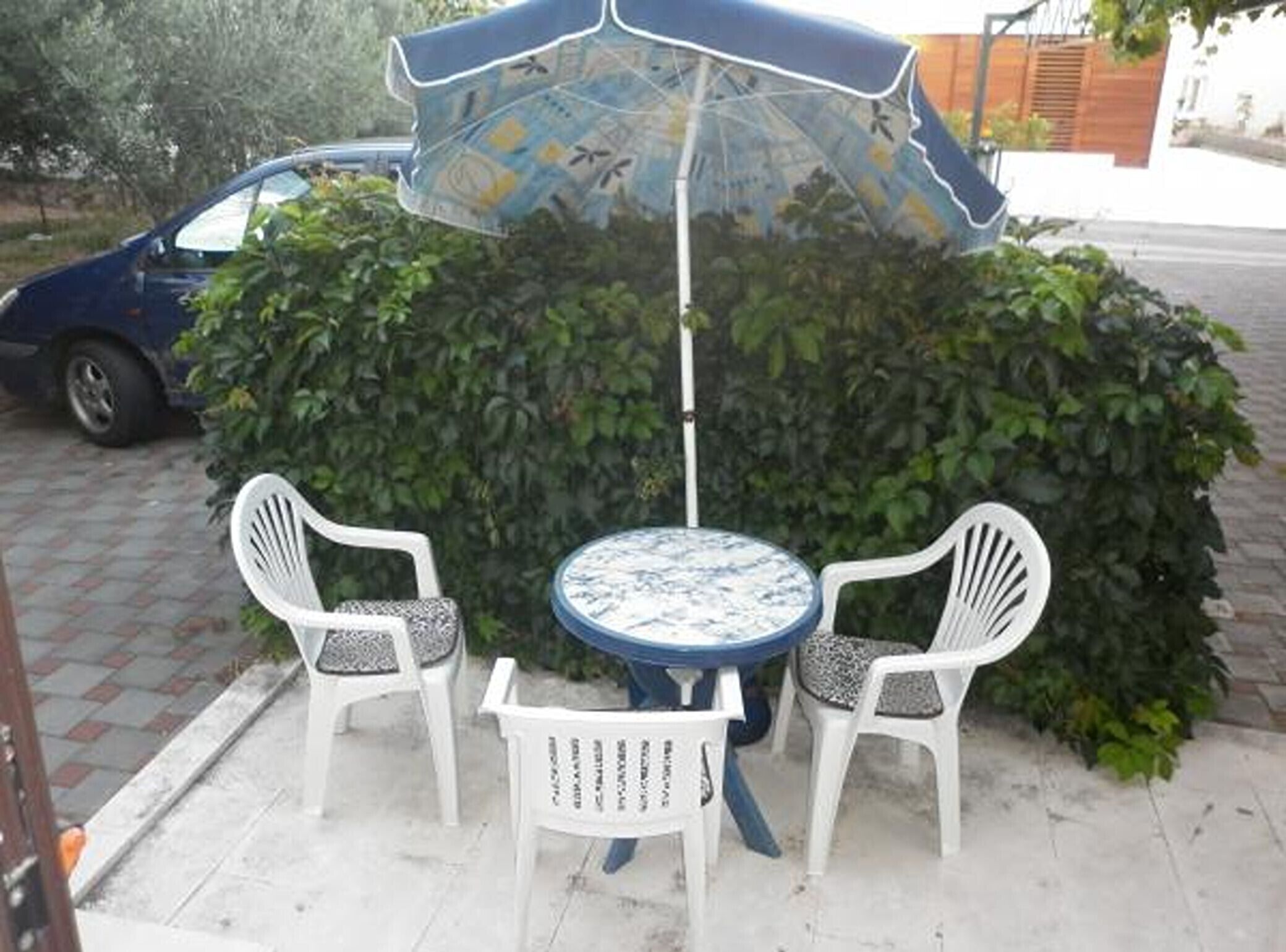 Een terras met een tafel, twee stoelen en een parasol, met een auto in de buurt.